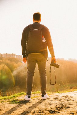 gün batımında elinde kamera ile tepenin üstünde duran adam