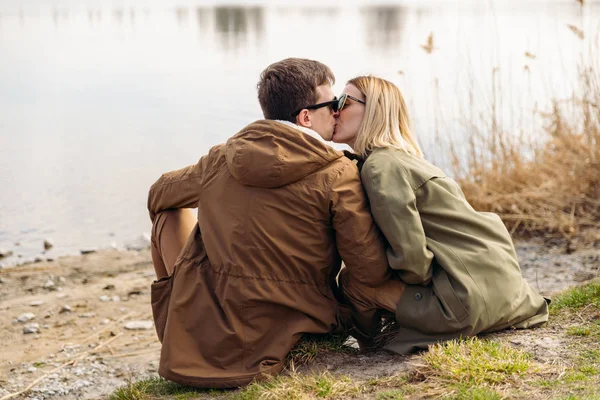 Casal bonito beijando na beira do rio sentado no chão — Fotografia de Stock