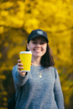 young pretty woman holding and showing yellow coffee paper cup