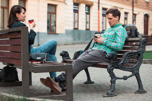communication problem man with woman sitting on bench at city street drinking coffee in paper cup looking ito phones