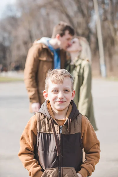 Smiling little boy in front. kissing parents on background — Stock Photo, Image
