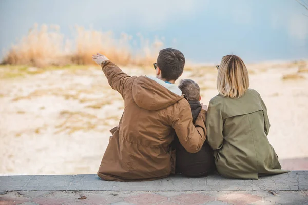 Jonge mooie familie zittend op het strand met uitzicht op het meer — Stockfoto