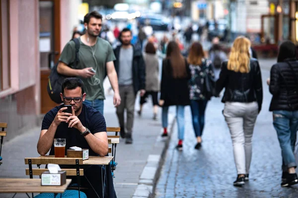LVIV, UKRAINE - 25 de abril de 2019: homem bebendo cerveja no café da rua da cidade olhando para o telefone — Fotografia de Stock