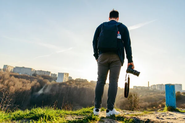 man standing on the top of the hill with camera in hands on sunset