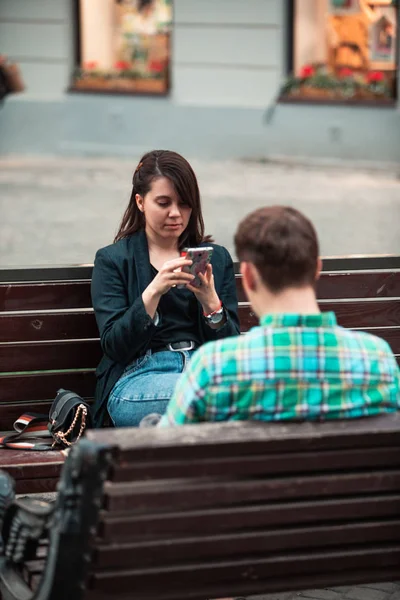 Πρόβλημα επικοινωνίας άντρας με γυναίκα που κάθεται στο παγκάκι στο δρόμο της πόλης πίνοντας καφέ σε χάρτινο κύπελλο ψάχνοντας για τηλέφωνα — Φωτογραφία Αρχείου