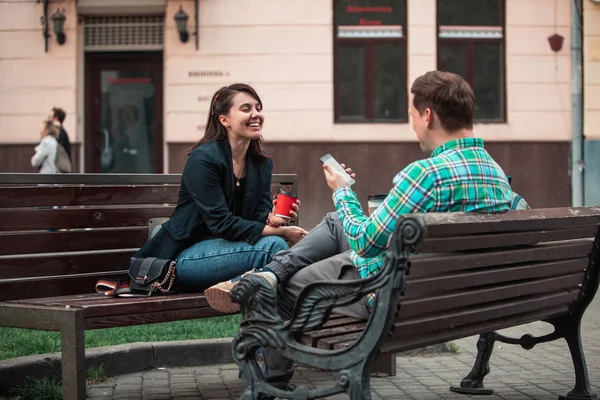 Internette kahve sörf içme bankta oturan kadın ile gülen konuşan adam. kentsel yaşam tarzı — Stok fotoğraf