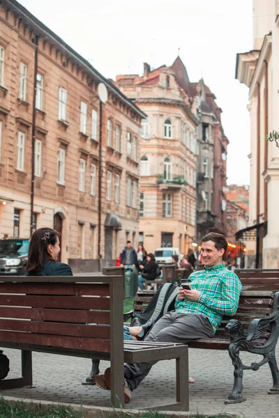 Γελώντας ο άνθρωπος με τη γυναίκα κάθεται στο παγκάκι πίνοντας καφέ σέρφινγκ στο διαδίκτυο. αστικός τρόπος ζωής — Φωτογραφία Αρχείου