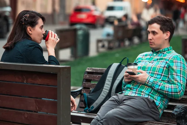 Hymyilevä pari istuu penkillä puhumassa toisilleen kahvin juomisesta — kuvapankkivalokuva