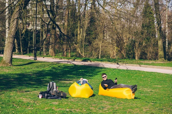 Dos amigos de los hombres que ponen en el colchón inflable amarillo que lee los libros que navegan Internet — Foto de Stock