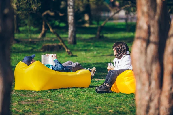 Pareja que pone en colchón inflable amarillo en el parque de la ciudad. libro de lectura. batidos para beber — Foto de Stock