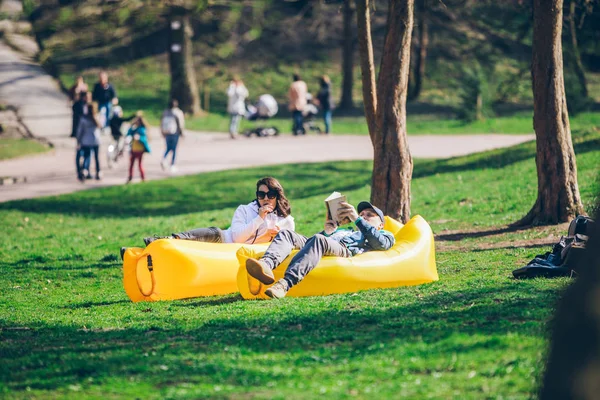 도시 공원에서 노란색 풍선 매트리스에 누워 커플. 책을 읽는. 마시는 스무디 — 스톡 사진