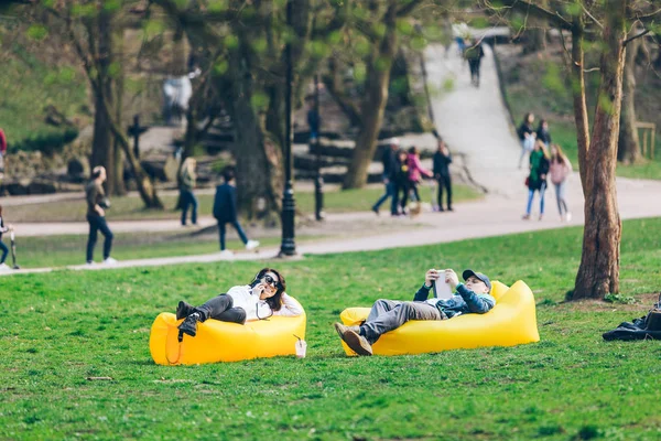 Пара, лежащая на жёлтом надувном матрасе в городском парке. чтение книги. телефон для серфинга — стоковое фото