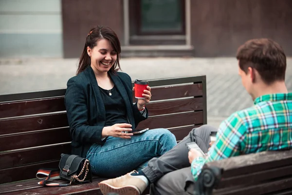 Sonriente pareja sentado en el banco hablando entre sí beber café — Foto de Stock