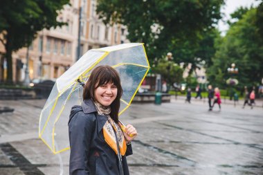 woman walking by wet rainy streets under transparent umbrella
