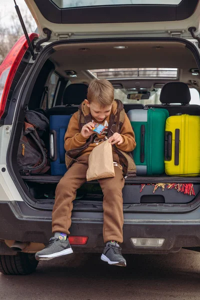 Маленька дитина дивиться в паперовий мішок з цукерками, сидячи в багажнику автомобіля — стокове фото