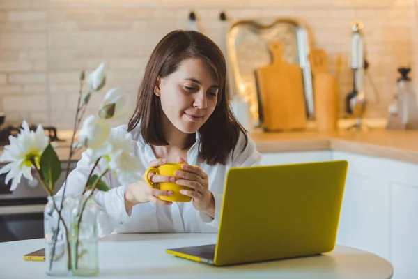 Jovem muito caucasiano mulher falando no telefone sentado na frente de laptop na cozinha — Fotografia de Stock