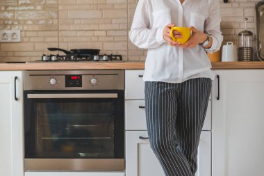 Mutfakta elinde sarı bardakla duran bir kadın.