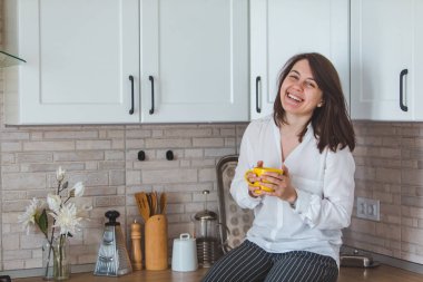 Genç ve güzel bir kadın mutfakta sarı bardaktan çay içiyor.