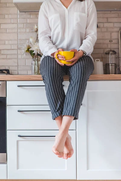 Mujer sentada en la mesa de la cocina con teléfono y taza amarilla — Foto de Stock