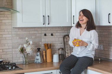 Genç ve güzel bir kadın mutfakta sarı bardaktan çay içiyor.