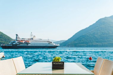 güzel bir deniz ve dağ manzarası ile sahilde Cafe tablo. üzerinde ayrılmış plaka. Cruise liner arka plan üzerinde
