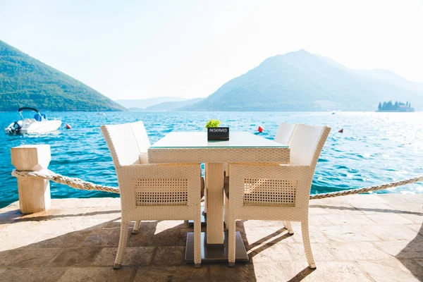 海と山の美しい景色とビーチのカフェ テーブル。その上に予約済みプレート — ストック写真