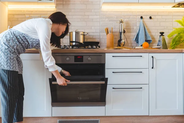 Wanita cantik muda membuka oven untuk memasak. konsep dapur domestik — Stok Foto