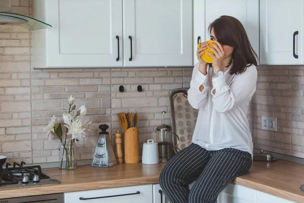 Jovem mulher bonita beber chá de caneca amarela na cozinha — Fotografia de Stock