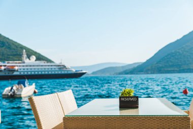 güzel bir deniz ve dağ manzarası ile sahilde Cafe tablo. üzerinde ayrılmış plaka. Cruise liner arka plan üzerinde
