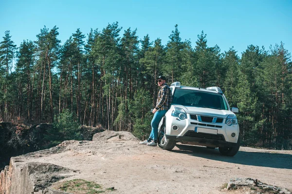 Joven de pie cerca de coche suv blanco en el bosque — Foto de Stock