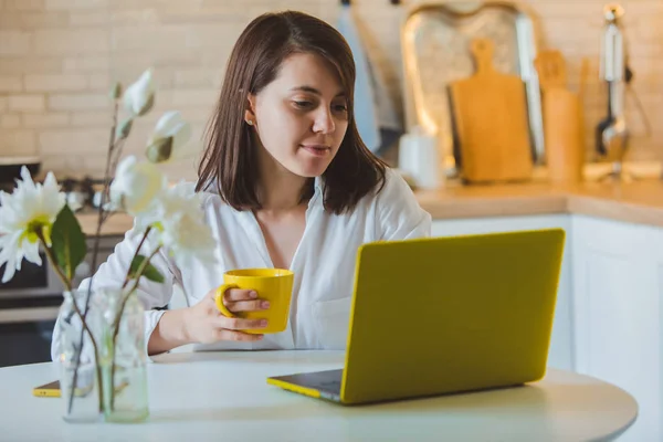 Young pretty caucasian woman talking on the phone sitting in front of laptop in the kitchen — Stock Photo, Image