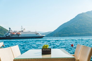 güzel bir deniz ve dağ manzarası ile sahilde Cafe tablo. üzerinde ayrılmış plaka. Cruise liner arka plan üzerinde
