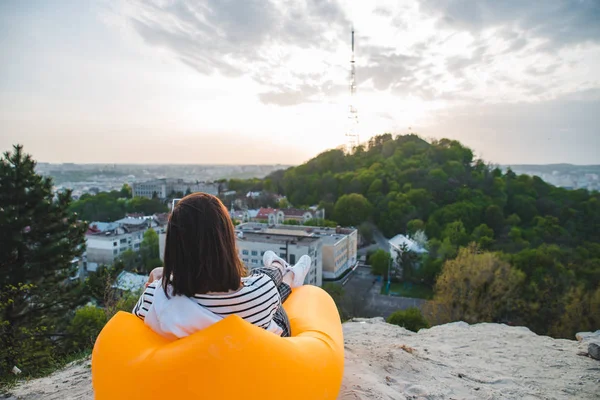 Frau sitzt auf gelber aufblasbarer Matratze und trinkt Kaffee und genießt den Sonnenuntergang über der Stadt — Stockfoto