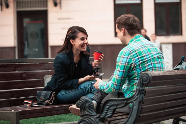 Smiling couple sitting on bench talking to each other drinking coffee — Stock Photo, Image