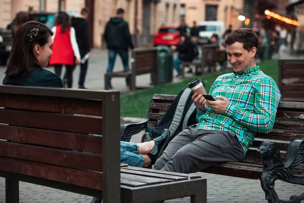 Rindo falando homem com mulher sentada no banco bebendo café surfando na internet. estilo de vida urbano — Fotografia de Stock