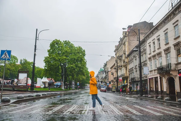 Женщина посреди улицы переходит дорогу в желтом плаще — стоковое фото