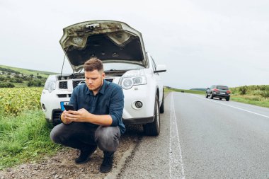 adam telefon ile kırık arabanın yanında oturan, yardım arıyor