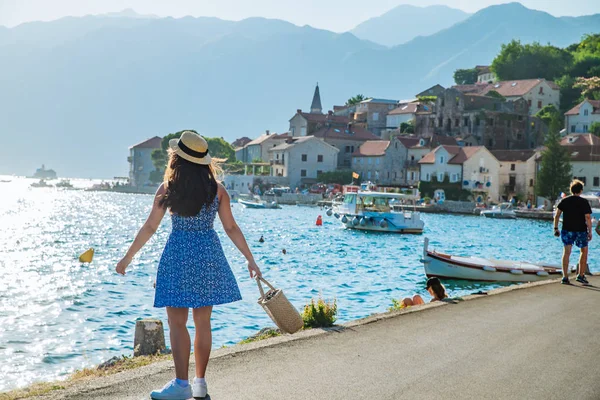 Giovane bella donna alla moda a piedi dalla banchina della città. mare e montagne sullo sfondo — Foto Stock