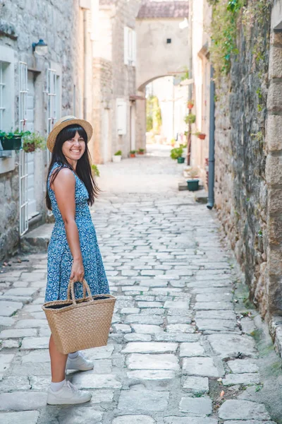 Woman walking by small perast streets in hat and blue dress — Stockfoto