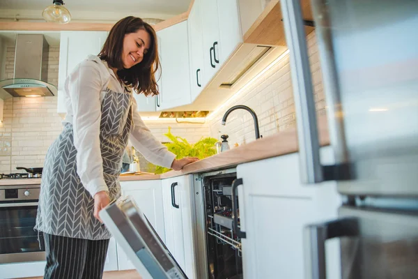 Молодая красивая женщина кладет посуду в посудомоечную машину — стоковое фото