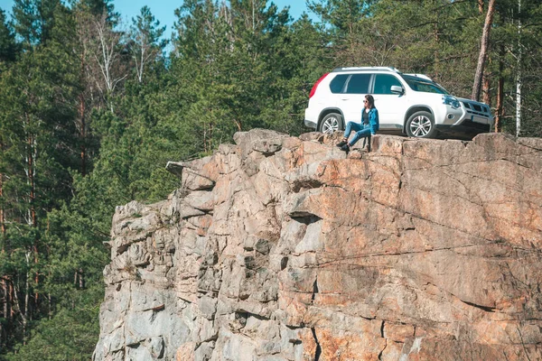 Donna seduta sulla scogliera con bella vista nella giornata di sole. suv auto sullo sfondo — Foto Stock