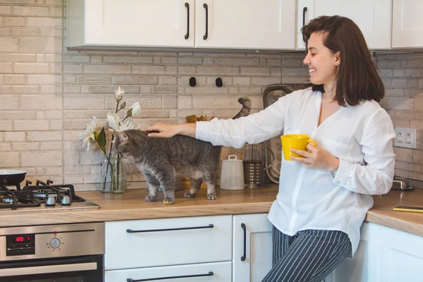 woman pet the cat and drinking tea at the kitchen