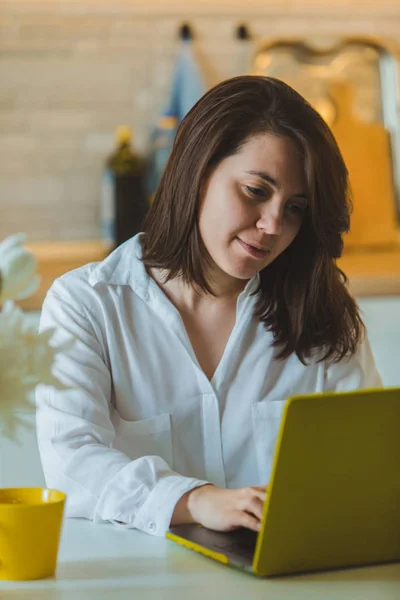 Young pretty caucasian woman talking on the phone sitting in front of laptop in the kitchen — Stock Photo, Image