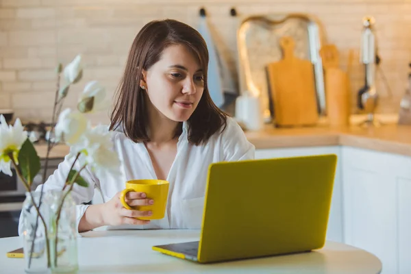 Young pretty caucasian woman talking on the phone sitting in front of laptop in the kitchen — Stock Photo, Image