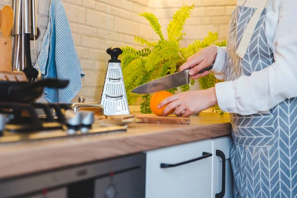 Mujer cortando naranja en la cocina doméstica — Foto de Stock