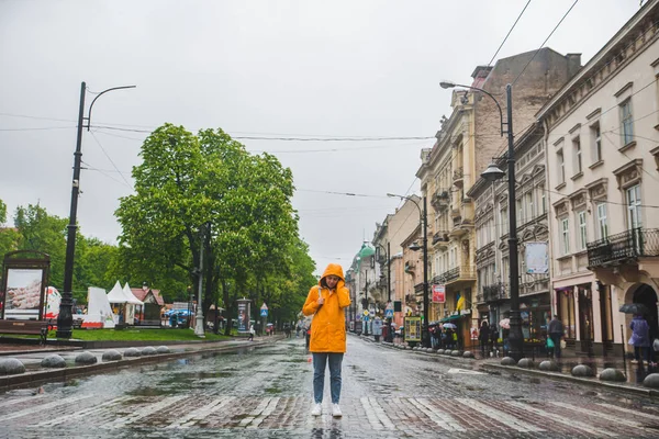 Жінка посеред вулиці, що перетинає дорогу в жовтому плащі — стокове фото
