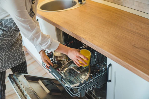 Молодая красивая женщина кладет посуду в посудомоечную машину — стоковое фото