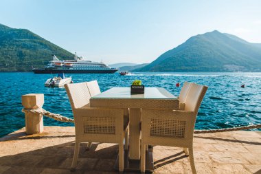 güzel bir deniz ve dağ manzarası ile sahilde Cafe tablo. üzerinde ayrılmış plaka. Cruise liner arka plan üzerinde