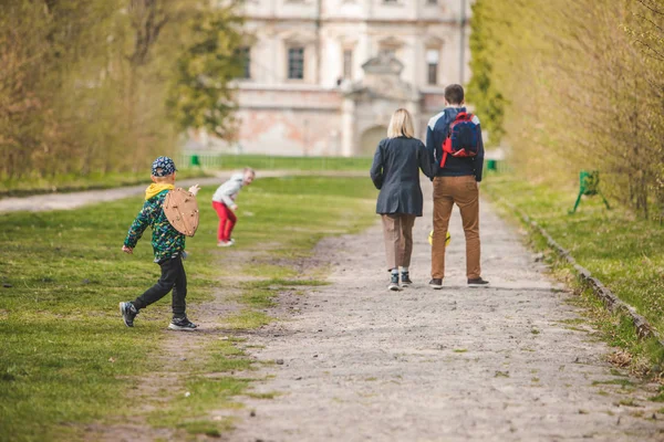 Діти грають з м'ячем і дерев'яним щитом батьки ходять по алеї — стокове фото