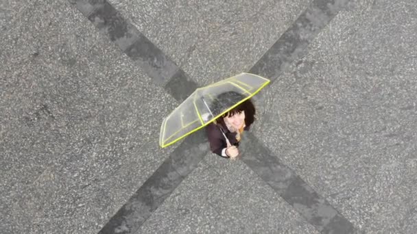Jonge mooie vrouw op het stadsplein met transparante gele paraplu glimlachen overhead uitzicht. — Stockvideo